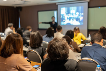 Back side of audience listening the Asian Speaker with casual suit on the stage in front of the room in the conference hall, business and education concept